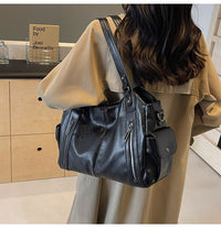 Sac cabas en cuir noir, bandoulière réglable, anses courtes, poches zippées visibles