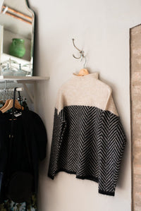 Pull col roulé en maille beige et noir, motif chevrons, porté sur cintre