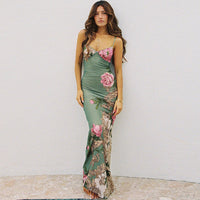 Robe longue verte à bretelles fines, fleurs roses et motifs feuillagés, près du corps.