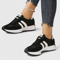 Baskets orthopédiques noires avec trois bandes blanches et semelle blanche.