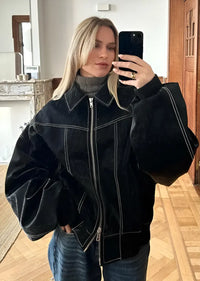 Veste en cuir oversize noire, fermeture zippée centrale et surpiqûres argentées.