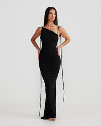 Robe longue noire près du corps, bretelles croisées, décolleté en V et liens pendants.
