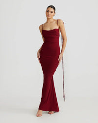 Robe longue rouge bordeaux près du corps, bretelles fines et franges pendantes.