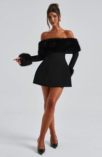 Robe courte noire à épaules dénudées, fausse fourrure épaulant le buste et manches fluides.